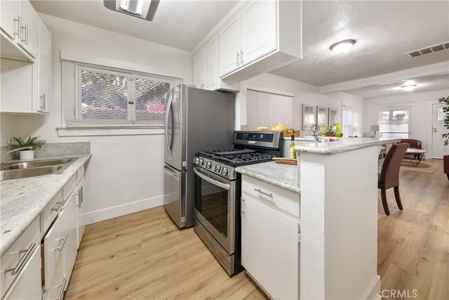 a kitchen with stainless steel appliances a stove a sink a refrigerator white cabinets and wooden floor