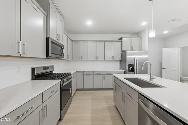 a kitchen with a sink dishwasher a stove top oven a refrigerator with white cabinets and wooden floor