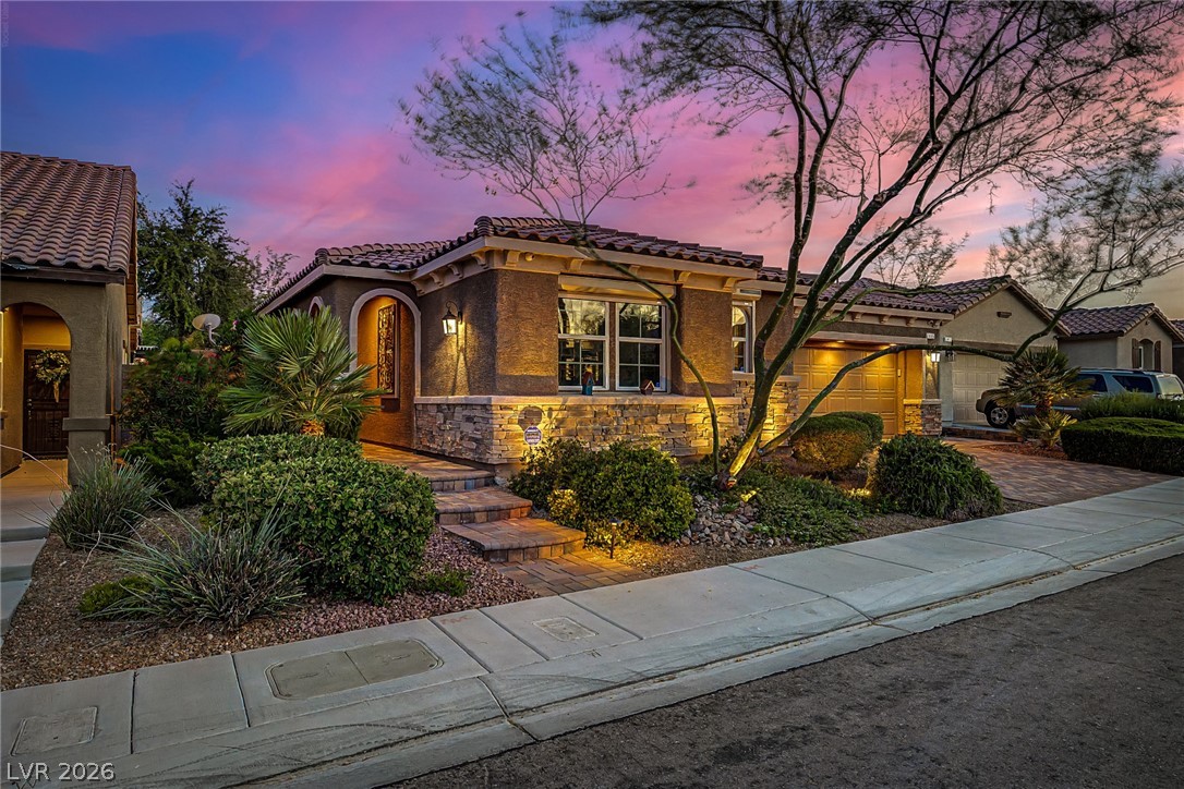7415 Campbell Ranch Avenue Las Vegas, NV 89179 - Photo 5 of 52 Stone veneer and a tile roof define this charming stucco home, illuminated by subtle landscaping lights.