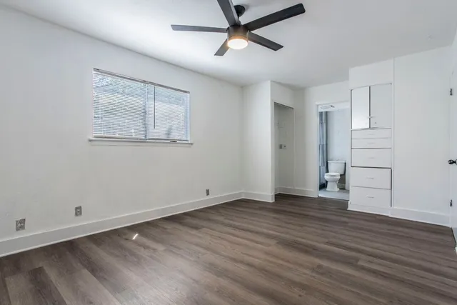 a view of an empty room with wooden floor and a ceiling fan