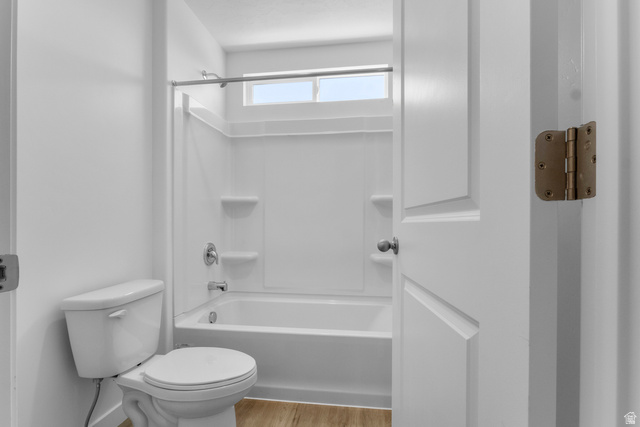 1355 West 2350 South, Unit 11 Perry, UT 84302 - Photo 24 of 39 Bathroom featuring a white tub and shower combination with an integrated storage shelf, a white toilet, and wood-finish flooring