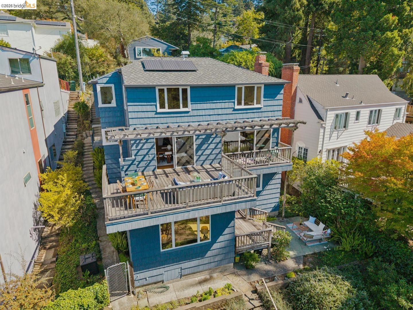 155 Avenida Drive Berkeley, CA 94708 - Photo 83 of 86 Multi-level exterior with blue siding, a multi-tiered deck with wood railing, a rooftop solar panel array, and an integrated pergola