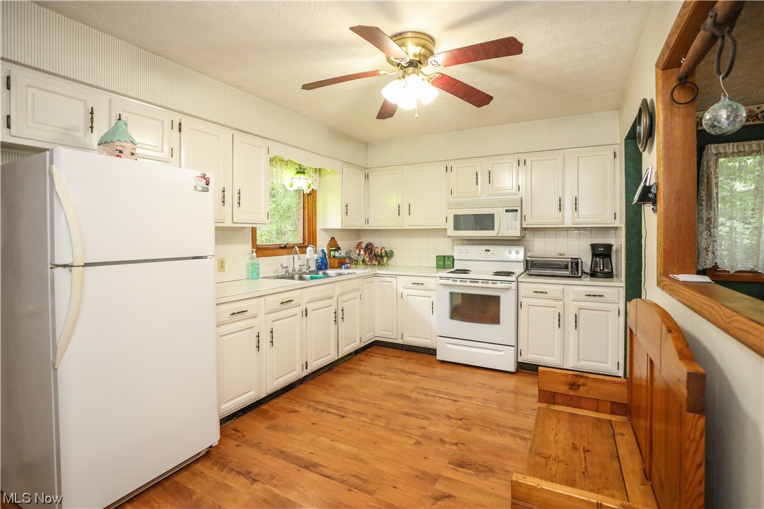 5344 Camp Road Ravenna, OH 44266 - Photo 10 of 30 Kitchen with white cabinets, a healthy amount of sunlight, white appliances, backsplash, light hardwood floors, and ceiling fan