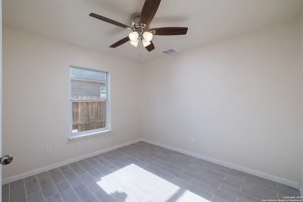 an empty room with wooden floor fan and windows
