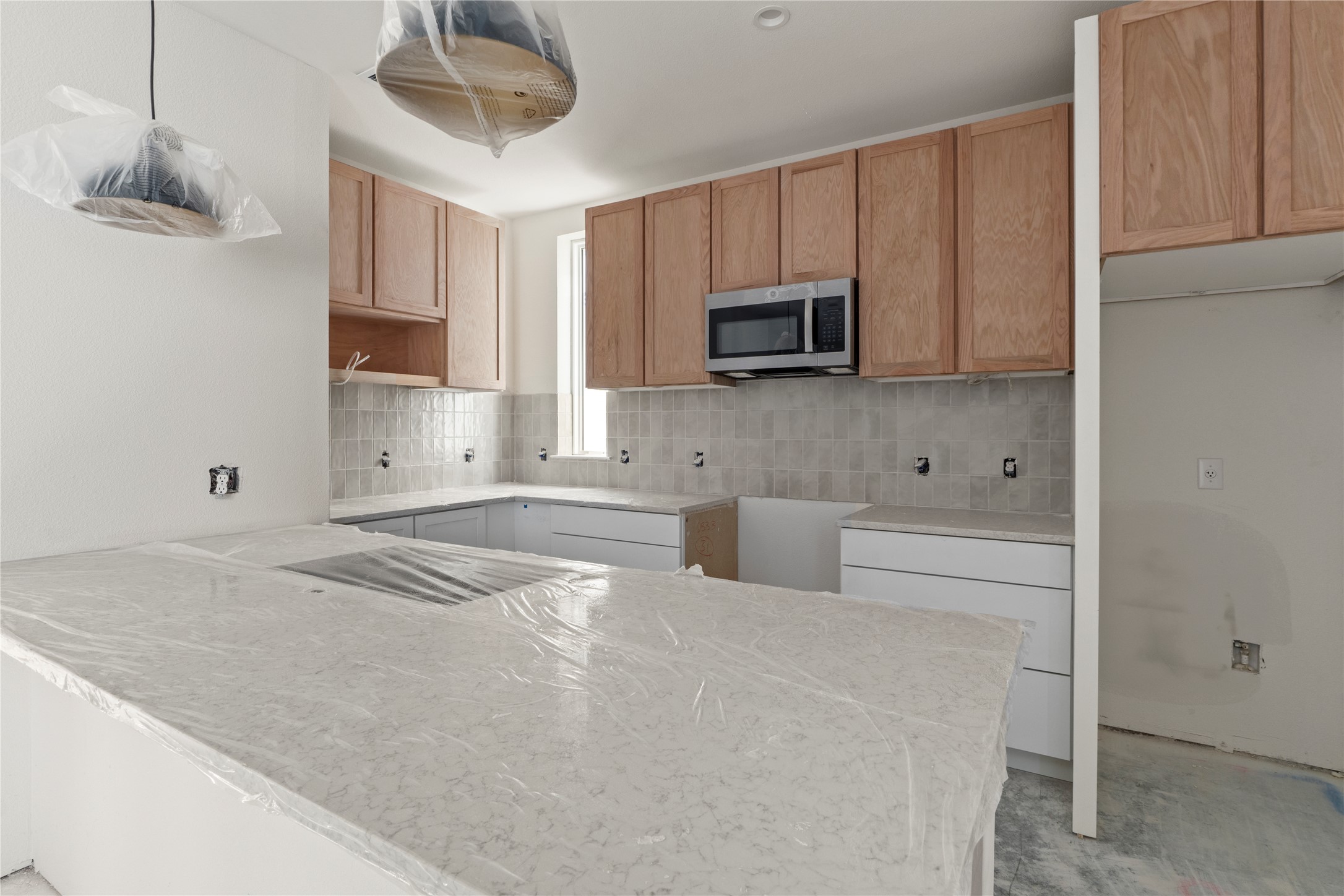 1180 Lott Avenue Austin, TX 78721 - Photo 3 of 40 Kitchen featuring a peninsula, stainless steel microwave, pendant lighting, decorative backsplash, and light stone counters