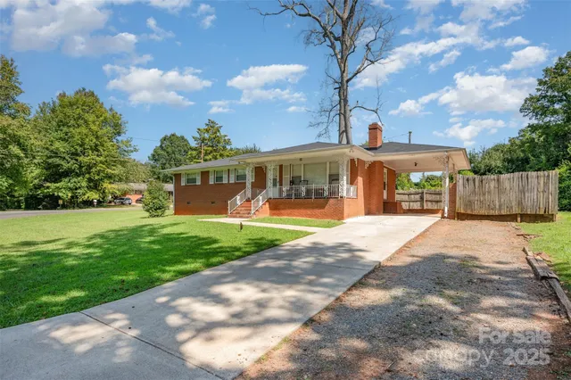 a view of a white house with a big yard plants and large tree