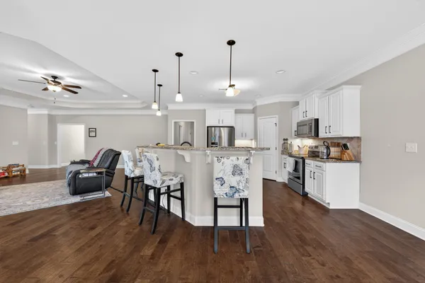 a open kitchen with stainless steel appliances granite countertop a stove a refrigerator a kitchen island a dining table and chairs with wooden floor