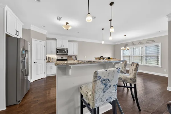 a kitchen with stainless steel appliances granite countertop a dining table chairs refrigerator and sink