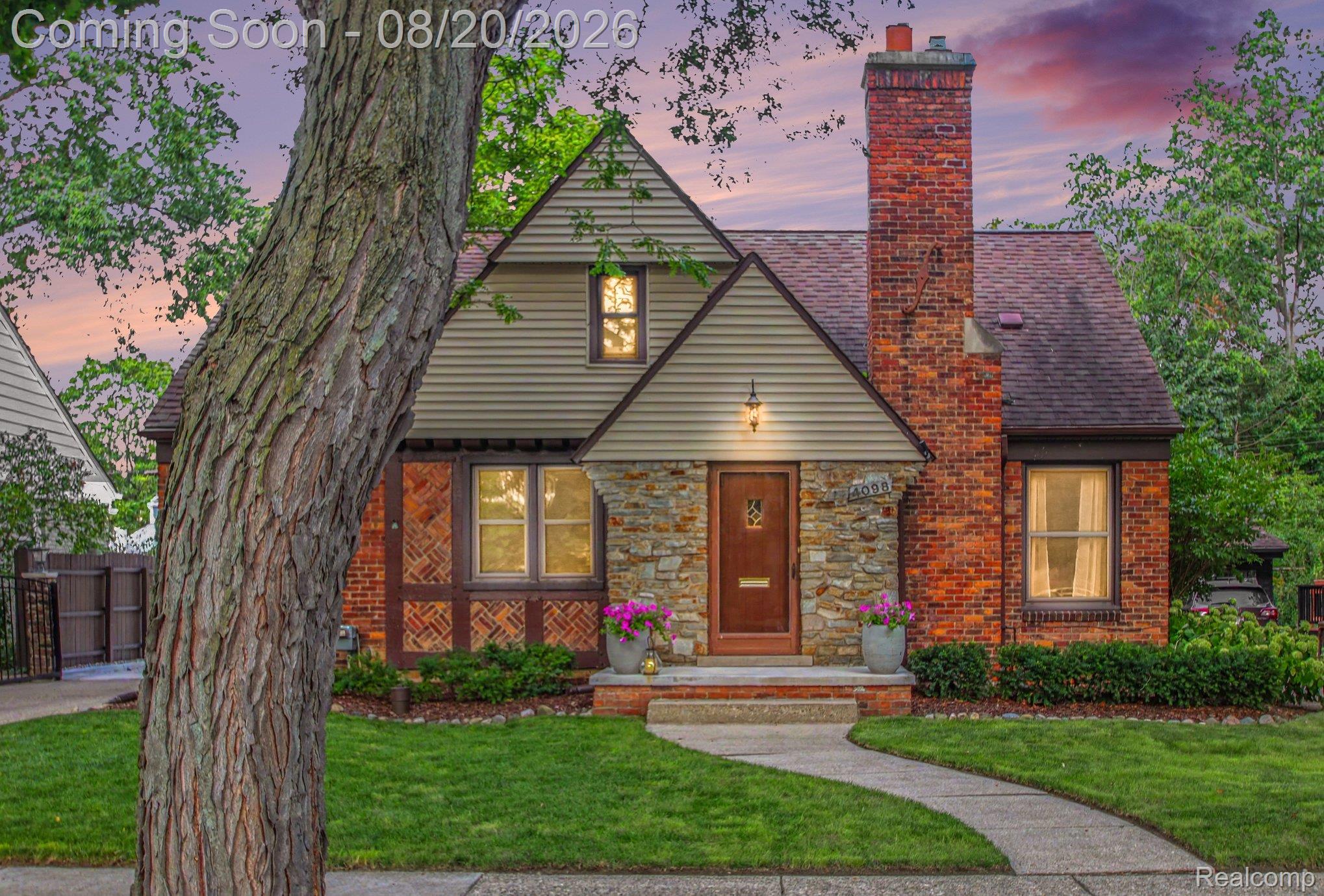 Gabled roofline, stone and brick facade, prominent brick chimney, arched entry door, and a curved concrete walkway