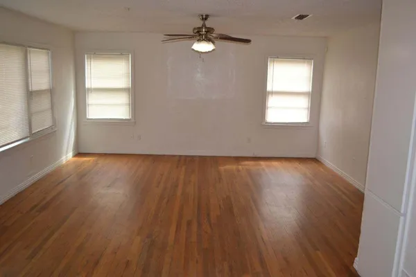 an empty room with wooden floor chandelier and windows