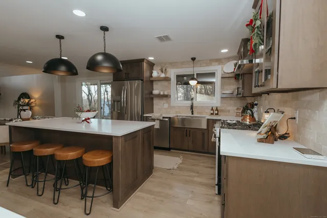 a kitchen with stainless steel appliances a sink a stove a refrigerator and chairs