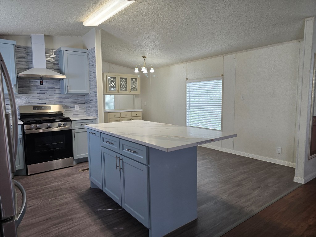 7628 Northview Lane Austin, TX 78724 - Photo 2 of 19 Kitchen with appliances with stainless steel finishes, wall chimney exhaust hood, hanging light fixtures, a kitchen island, and dark wood-style flooring