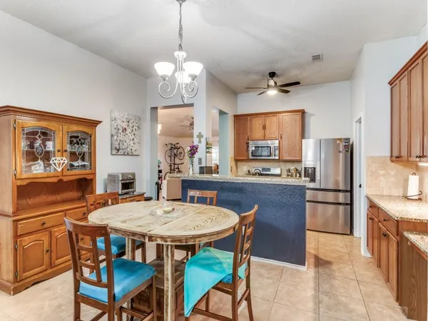 a kitchen with stainless steel appliances granite countertop a dining table chairs refrigerator and cabinets