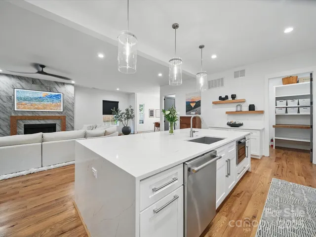 a large white kitchen with kitchen island a stove a sink a refrigerator and a dining table with wooden floor