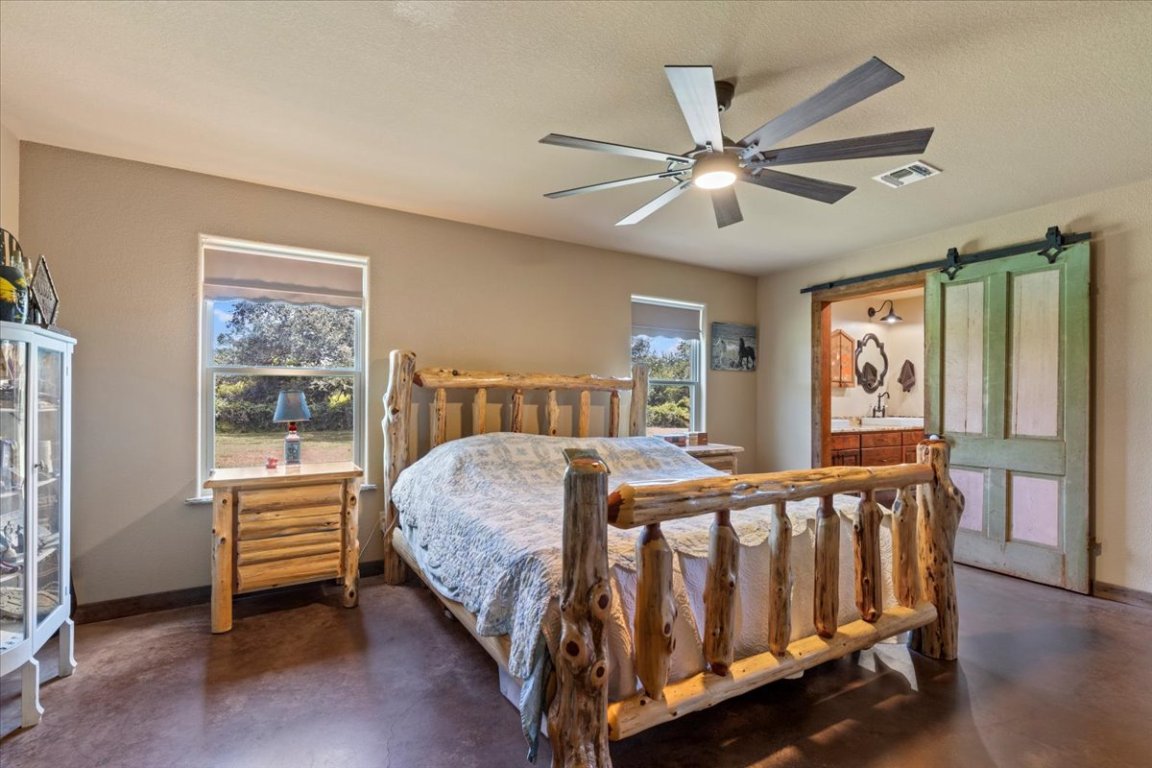 7835 Berger Road Schulenburg, TX 78956 - Photo 14 of 40 Bedroom with concrete floors, a textured ceiling, ensuite bathroom, a ceiling fan, and a barn door (Door from Leneski homestead)