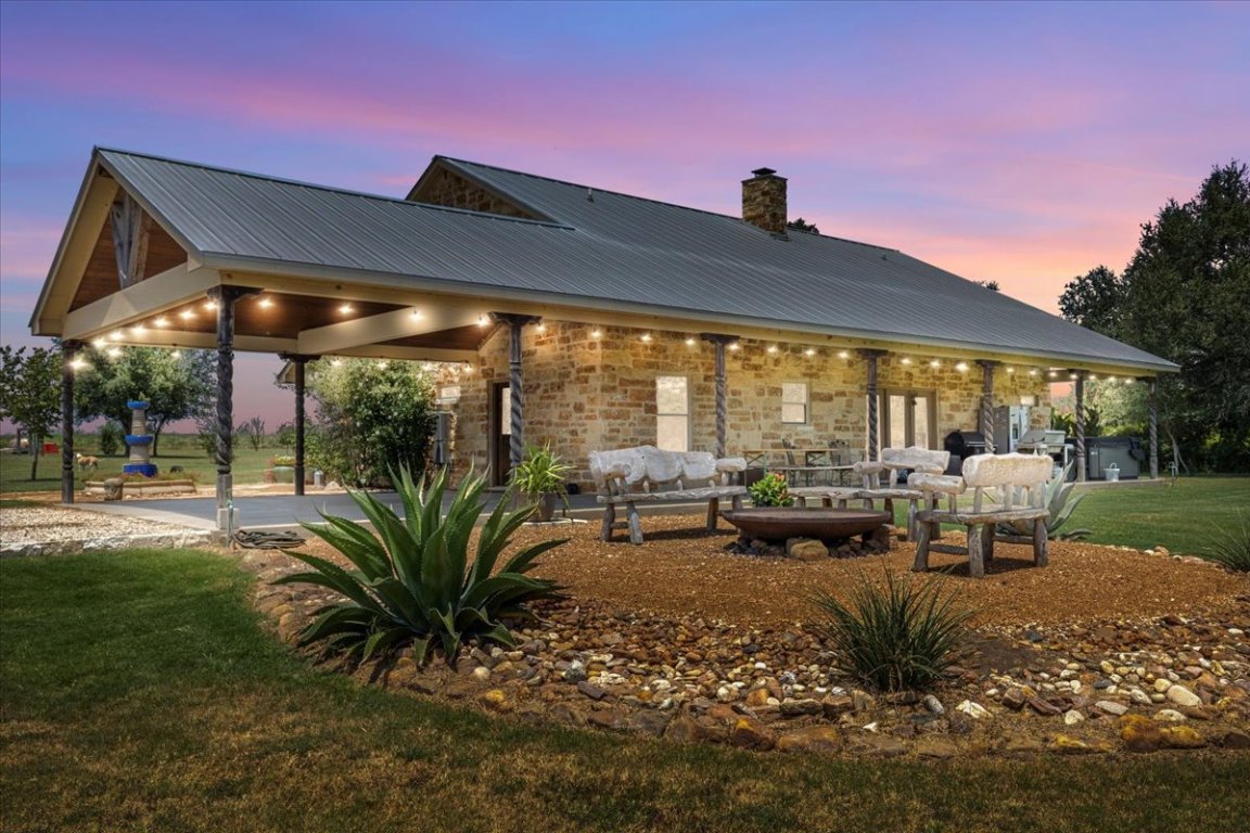 7835 Berger Road Schulenburg, TX 78956 - Photo 4 of 40 Back of property at dusk with a chimney, a lawn, a metal roof, stone siding, and a patio