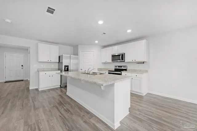 a kitchen with stainless steel appliances white cabinets a sink a stove a refrigerator and a microwave