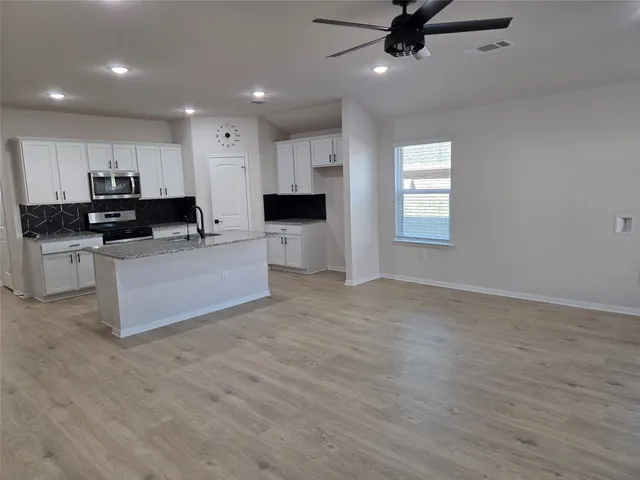 a living room with stainless steel appliances kitchen island granite countertop a stove a sink a refrigerator white cabinets and wooden floor