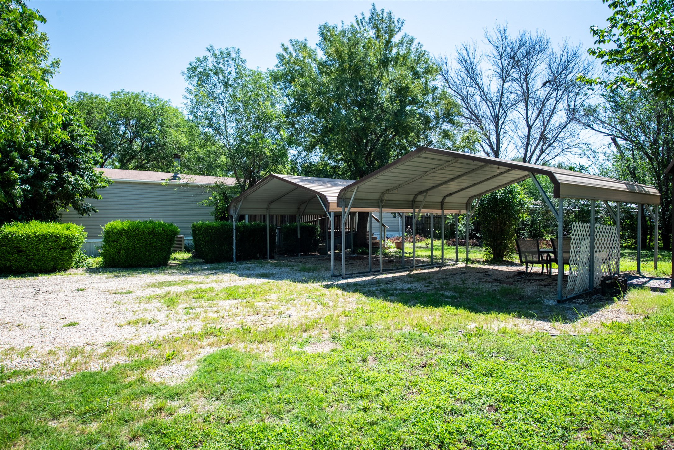 258 Quail Ridge Drive Kyle, TX 78640 - Photo 8 of 11 Expansive outdoor area featuring two multi-vehicle carports, a gravel parking pad, and mature trees