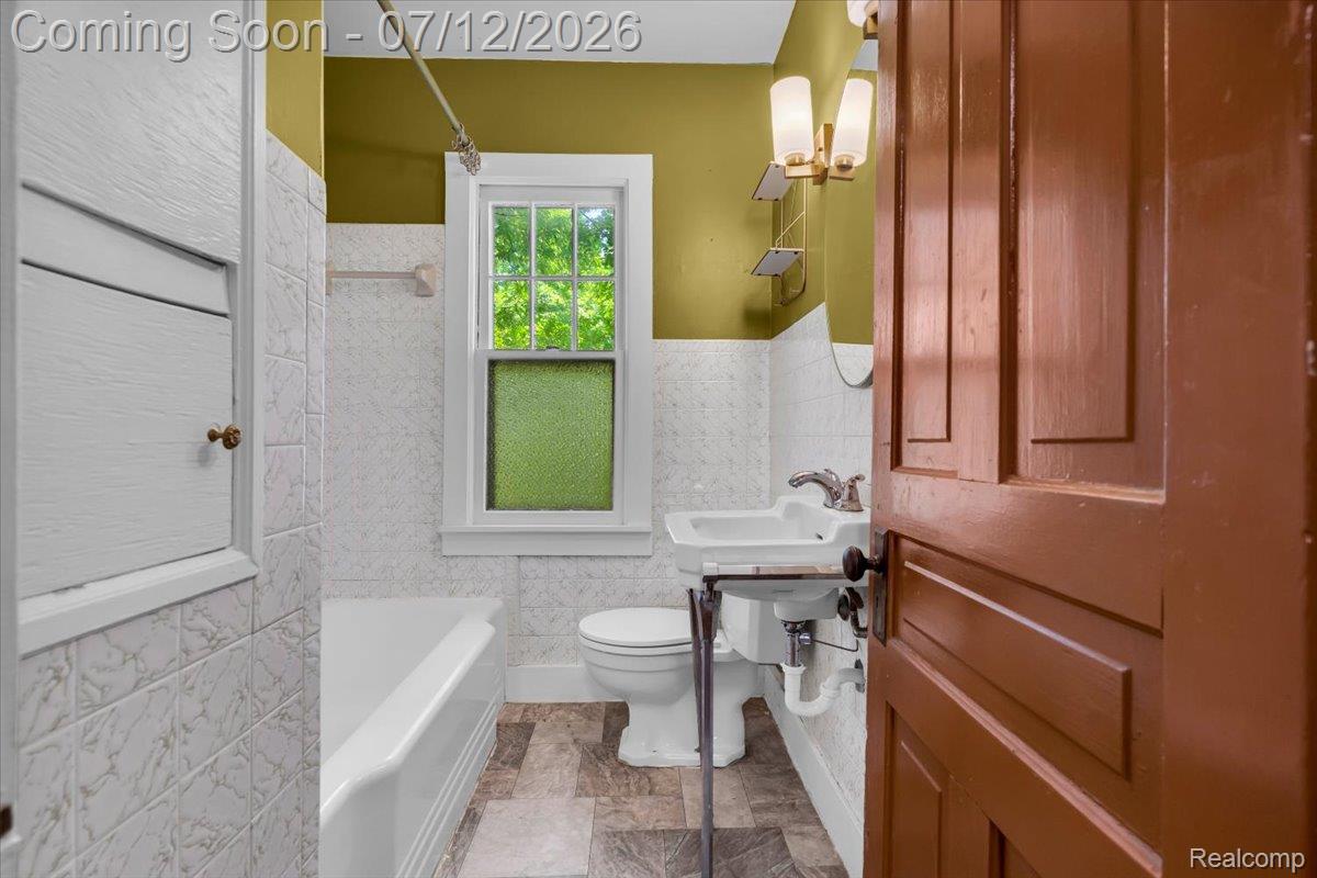 624 North Prospect Road Ypsilanti, MI 48198 - Photo 11 of 28 Bathroom featuring a white porcelain tub, pedestal sink, patterned floor tile, white wall tiling, and a window with privacy glass