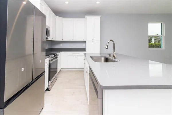 a kitchen with stainless steel appliances a sink a stove a microwave a refrigerator a sink and a cabinets