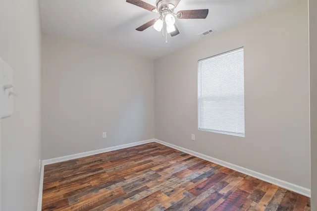 a view of empty room with wooden floor and fan