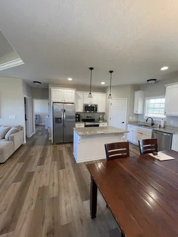 a kitchen with stainless steel appliances kitchen island granite countertop a stove a refrigerator a sink a dining table and chairs with wooden floor
