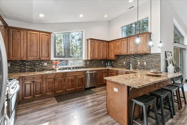 a kitchen with stainless steel appliances granite countertop wooden cabinets a sink dishwasher a stove and a refrigerator with wooden floor