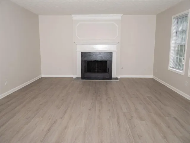 a view of an empty room with wooden floor fireplace and a window