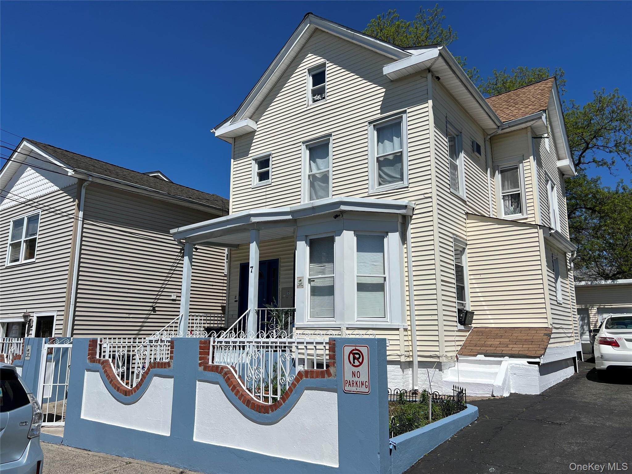 Cream-colored siding exterior featuring a covered porch with white railings, a bay window, and a gabled roofline