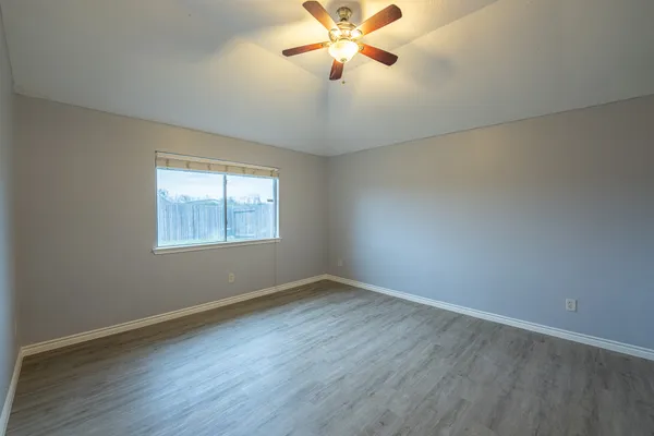 an empty room with wooden floor fan and windows