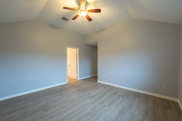 a view of an empty room with wooden floor and a ceiling fan