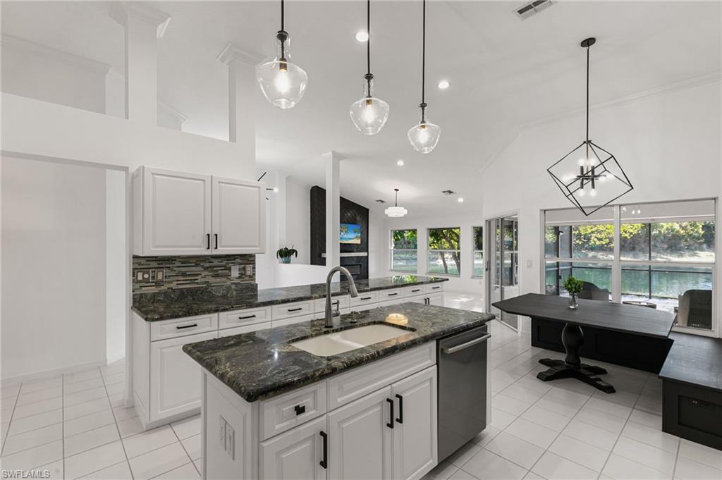 7867 Gardner Drive Naples, FL 34109 - Photo 11 of 36 Kitchen with white cabinetry, dark stone counters, an island with sink, light tile patterned flooring, and lofted ceiling