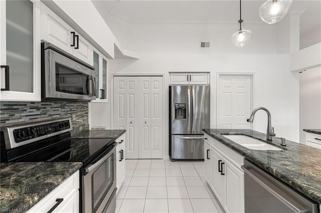 7867 Gardner Drive Naples, FL 34109 - Photo 13 of 36 Kitchen featuring stainless steel appliances, dark stone counters, decorative light fixtures, white cabinets, and ornamental molding