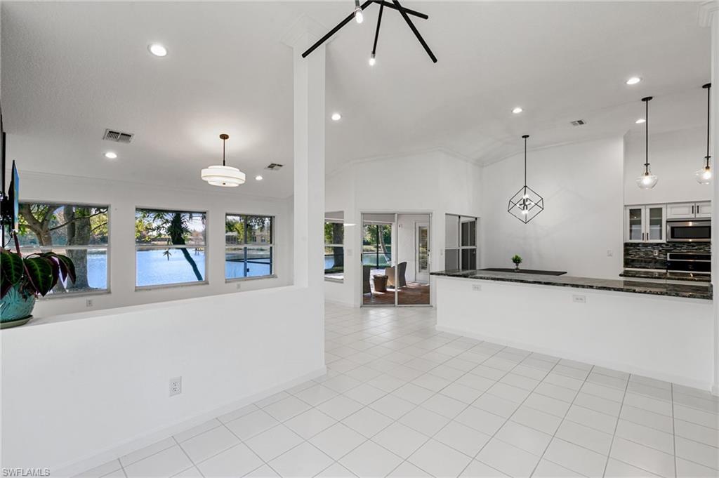 7867 Gardner Drive Naples, FL 34109 - Photo 4 of 36 Kitchen with vaulted ceiling, dark stone countertops, glass insert cabinets, hanging light fixtures, and light tile patterned floors