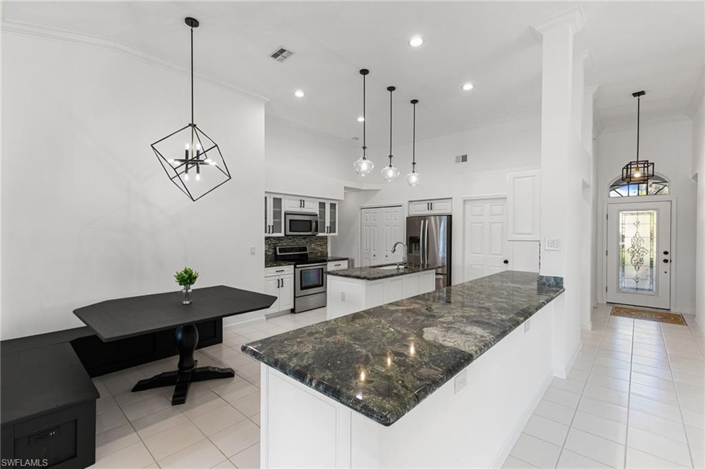 7867 Gardner Drive Naples, FL 34109 - Photo 8 of 36 Kitchen featuring suspended lighting, stainless steel appliances, glass insert cabinets, dark stone countertops, and an island with sink