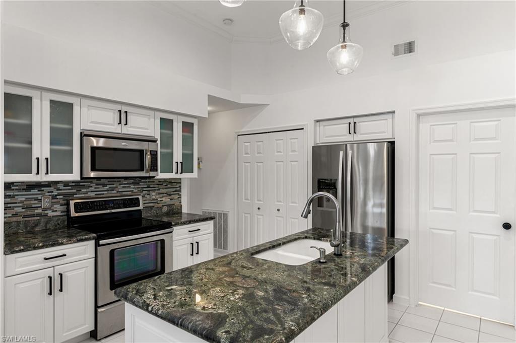 7867 Gardner Drive Naples, FL 34109 - Photo 9 of 36 Kitchen featuring stainless steel appliances, dark stone countertops, white cabinets, decorative light fixtures, and a center island with sink