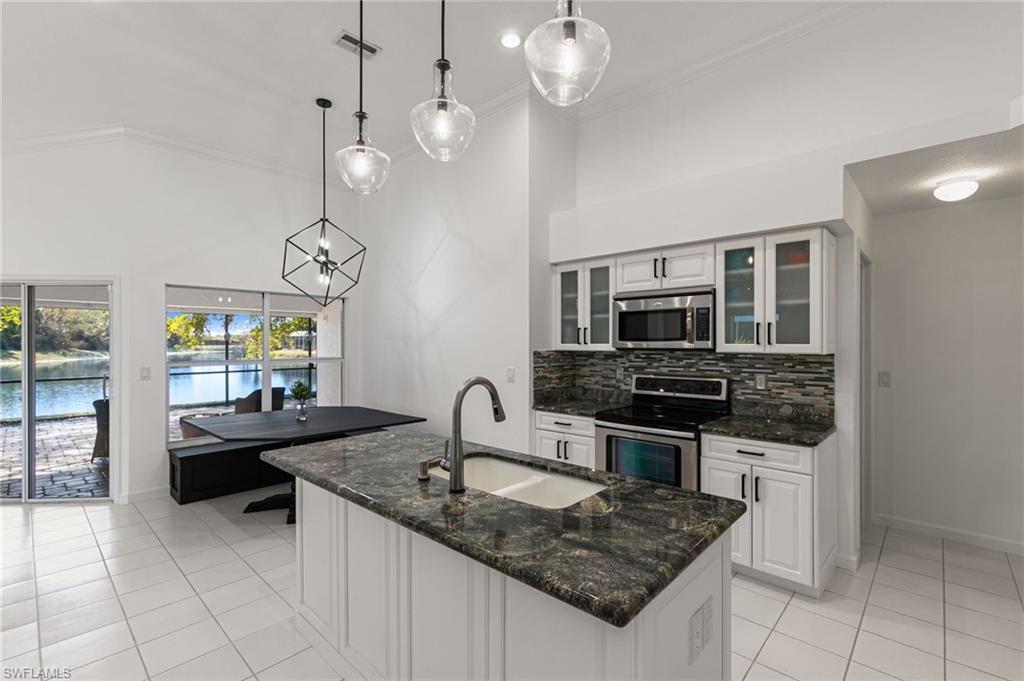 7867 Gardner Drive Naples, FL 34109 - Photo 10 of 36 Kitchen featuring white cabinetry, dark stone counters, stainless steel appliances, hanging light fixtures, and a high ceiling
