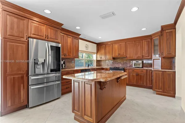 a kitchen with stainless steel appliances granite countertop a stove top oven a refrigerator and a sink with wooden cabinets