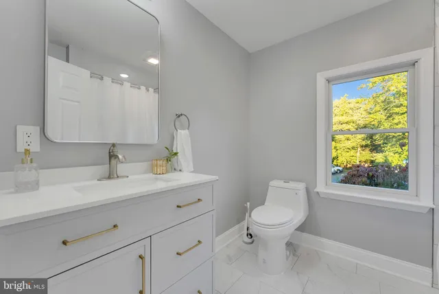 a bathroom with a toilet a sink a mirror a window and vanity