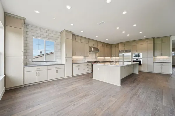a large white kitchen with center island and stainless steel appliances
