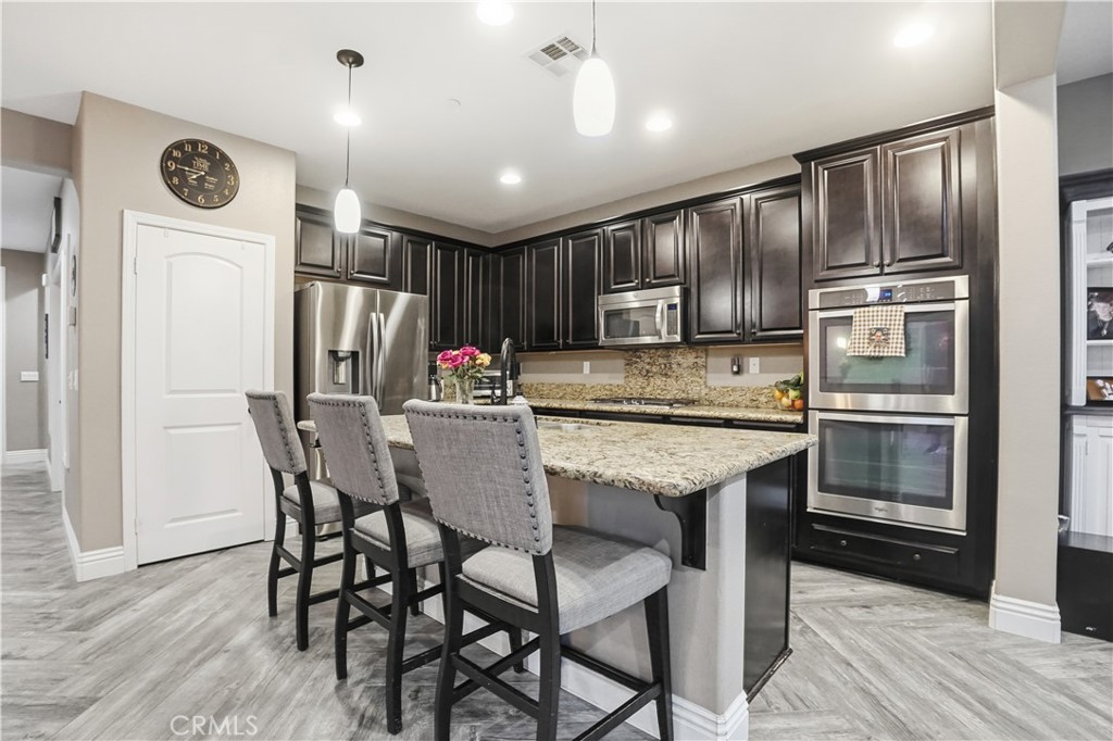 25654 Red Hawk Road Corona, CA 92883 - Photo 18 of 75 a kitchen with stainless steel appliances kitchen island granite countertop a refrigerator a stove microwave and island with wooden floor