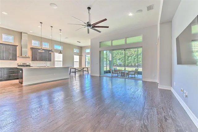 an empty room with wooden floor chandelier fan and windows