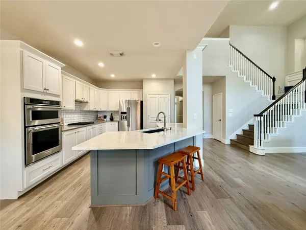 a kitchen with stainless steel appliances a microwave a stove a sink dishwasher a refrigerator and white cabinets with wooden floor