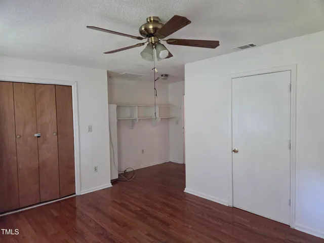 an empty room with wooden floor fan and windows