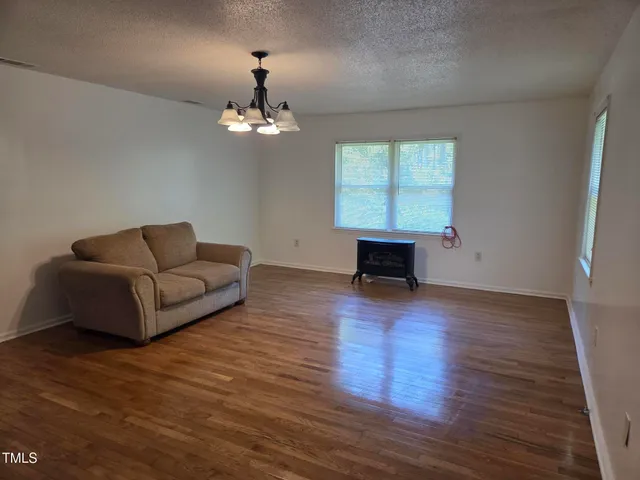 an empty room with wooden floor chandelier and windows