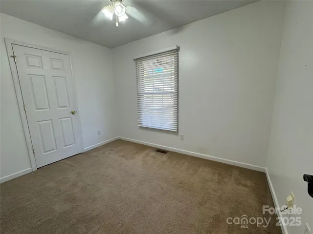 an empty room with a chandelier fan and windows