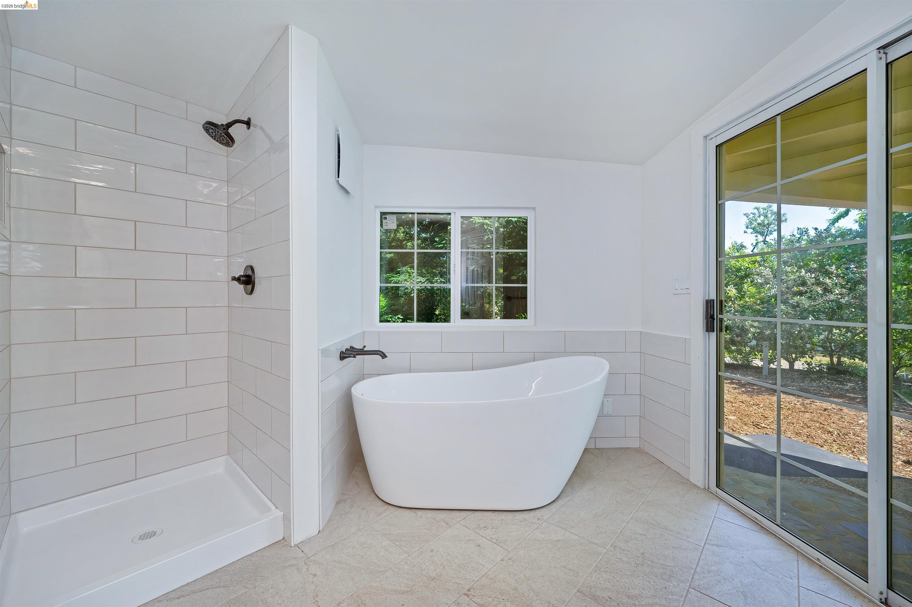 10474 Sheldon Road Elk Grove, CA 95624 - Photo 32 of 83 Modern bathroom featuring a freestanding soaking tub, separate shower with subway tile surround, matte black fixtures, grid-pane window, and sliding glass patio doors