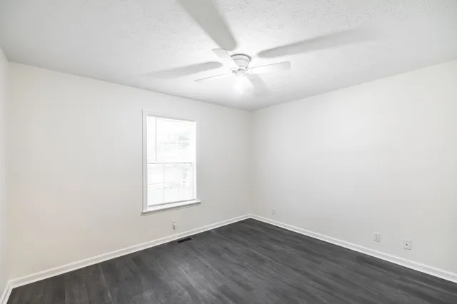an empty room with wooden floor fan and windows