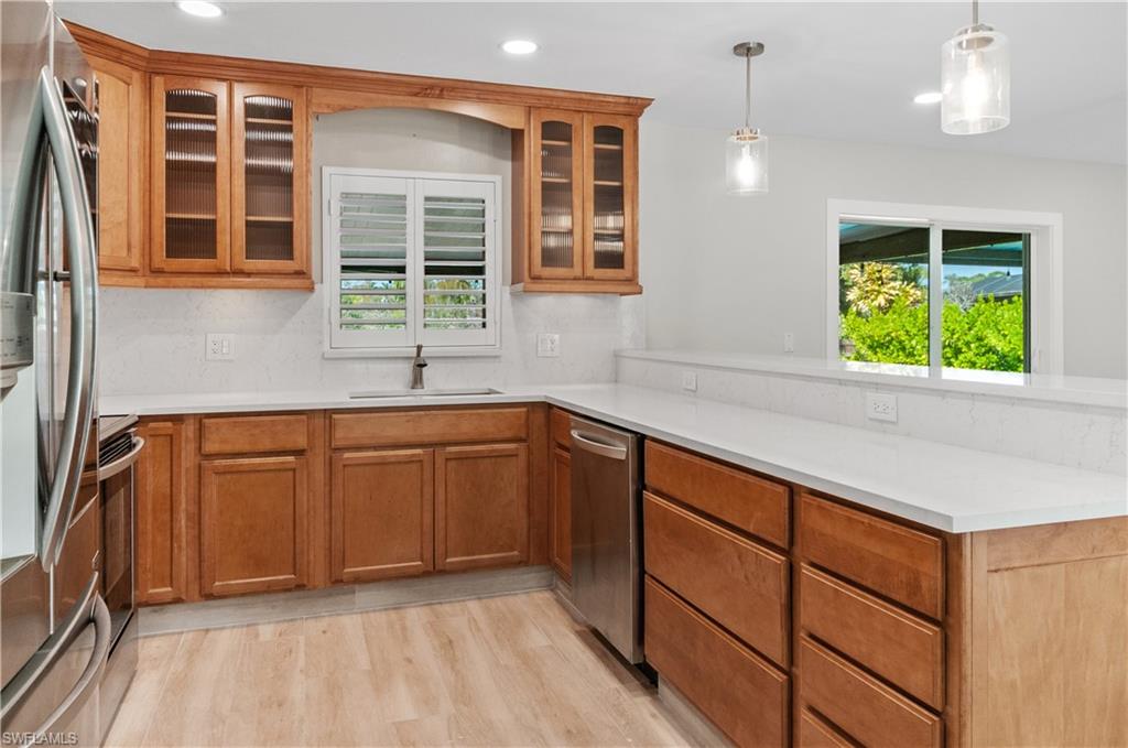 54 Liberty Lane Naples, FL 34112 - Photo 12 of 30 Kitchen with wood finish cabinetry, stainless steel appliances, hanging light fixtures, light wood-style floors, and a peninsula